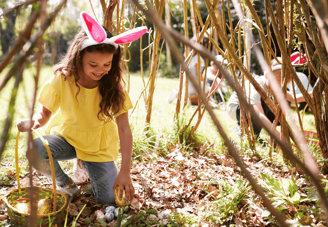 Group Of Children Wearing Bunny Ears Finding Easter Eggs Hidden In Garden
