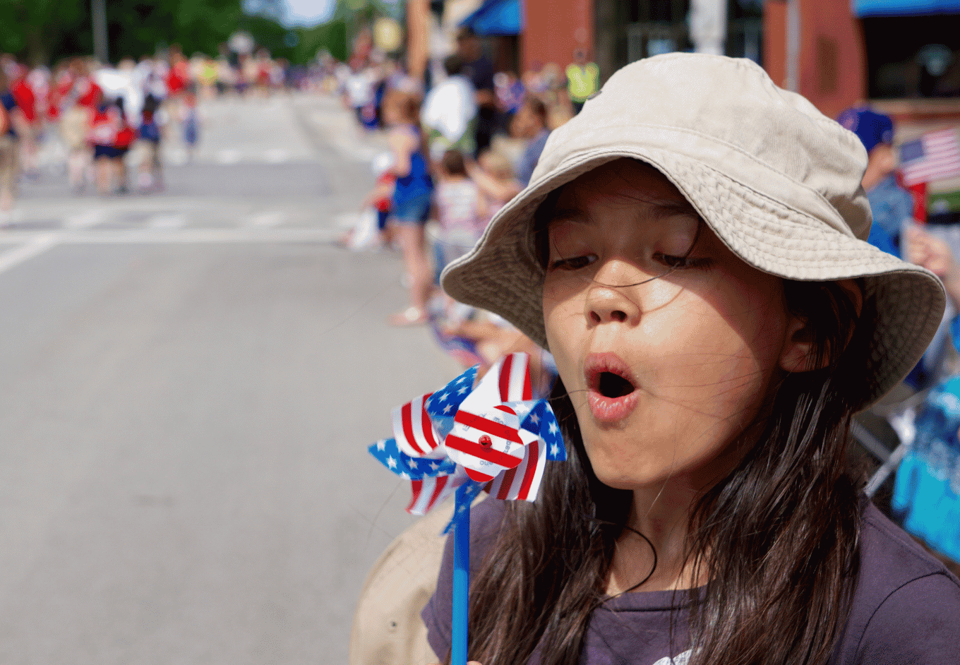 girl blows patriotic stars and stripes pinwheel at parade