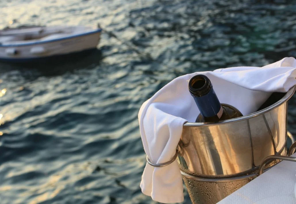 A bottle of wine in an ice bucket with the ocean and a boat in the background