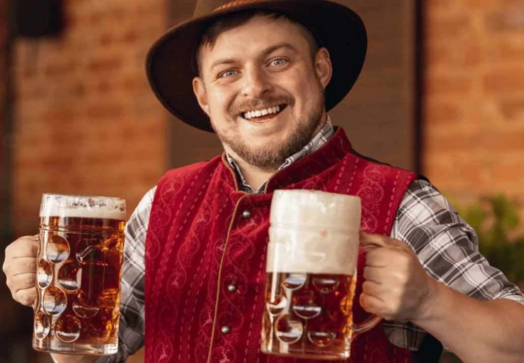 Happy smiling man, waiter in traditional Austrian or Bavarian costume holding mug, glass of dark