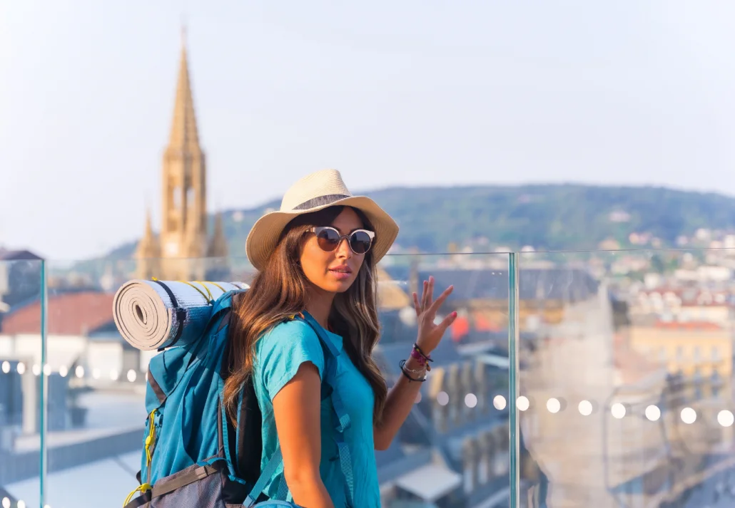 Young traveling tourist female in a hat and sunglasses with a backpack posing over a city view