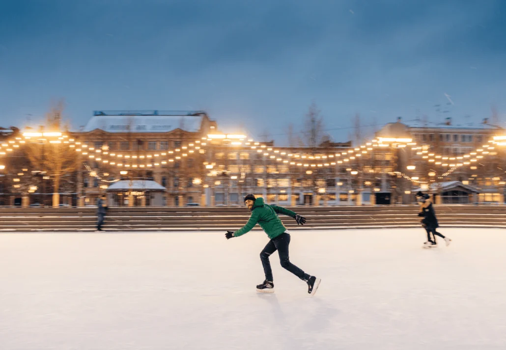 Man has fun in outdoor park on ice rink decorated with garlands, shows his talents of skating