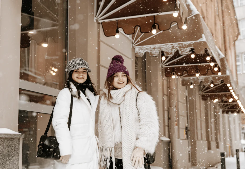 
Smiling women enjoying snowfall while standing outdoors