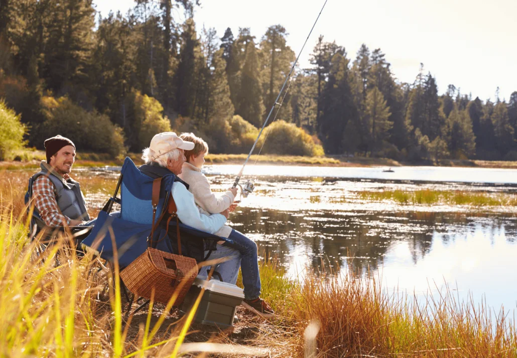 
Grandad teaches his grandson to fish at a lake, dad watching