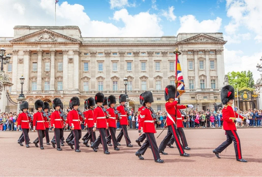 London Attractions - Some 20 guards marching in front of the Buckingham Palace while being watched by a crowd of people.