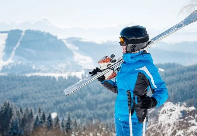A happy woman holding her ski equipments on top of a mountain.