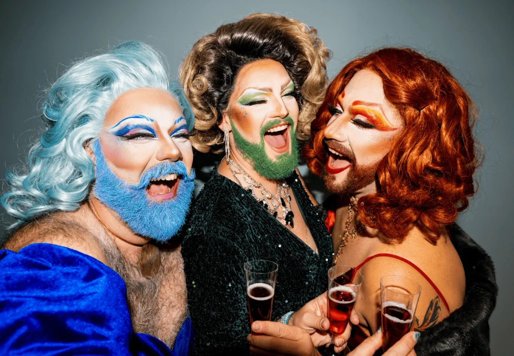 Three drag queens celebrating in style with toasting wine glasses
