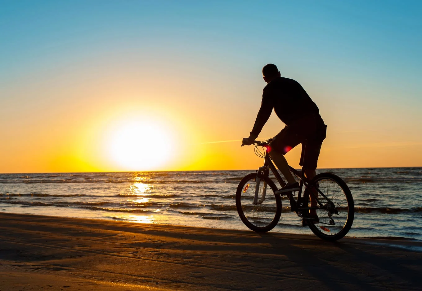 A man cyclist on the beach during the sunset. 